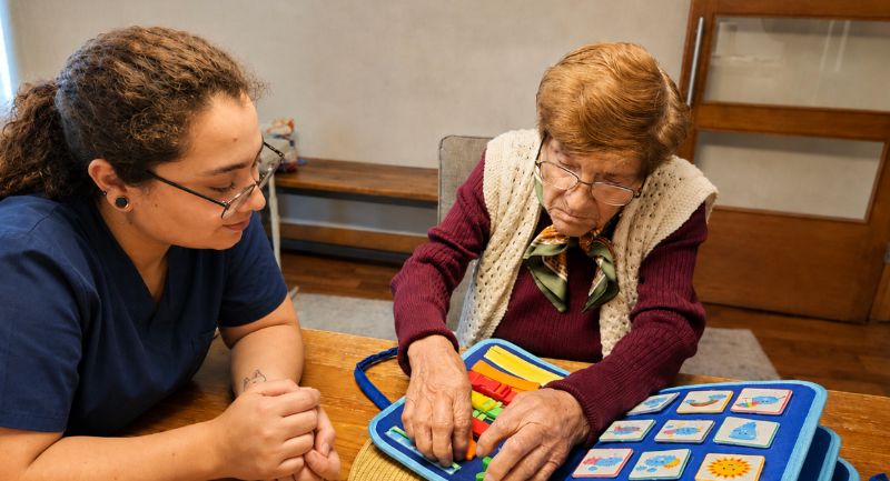 Taller de memoria en el centro de día Nuestras Raíces: una cuidadora acompaña a una persona mayor con un juego cognitivo